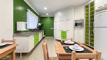 A modern kitchen with white cabinets, a green accent wall, a dining table with chairs, and a built-in microwave.