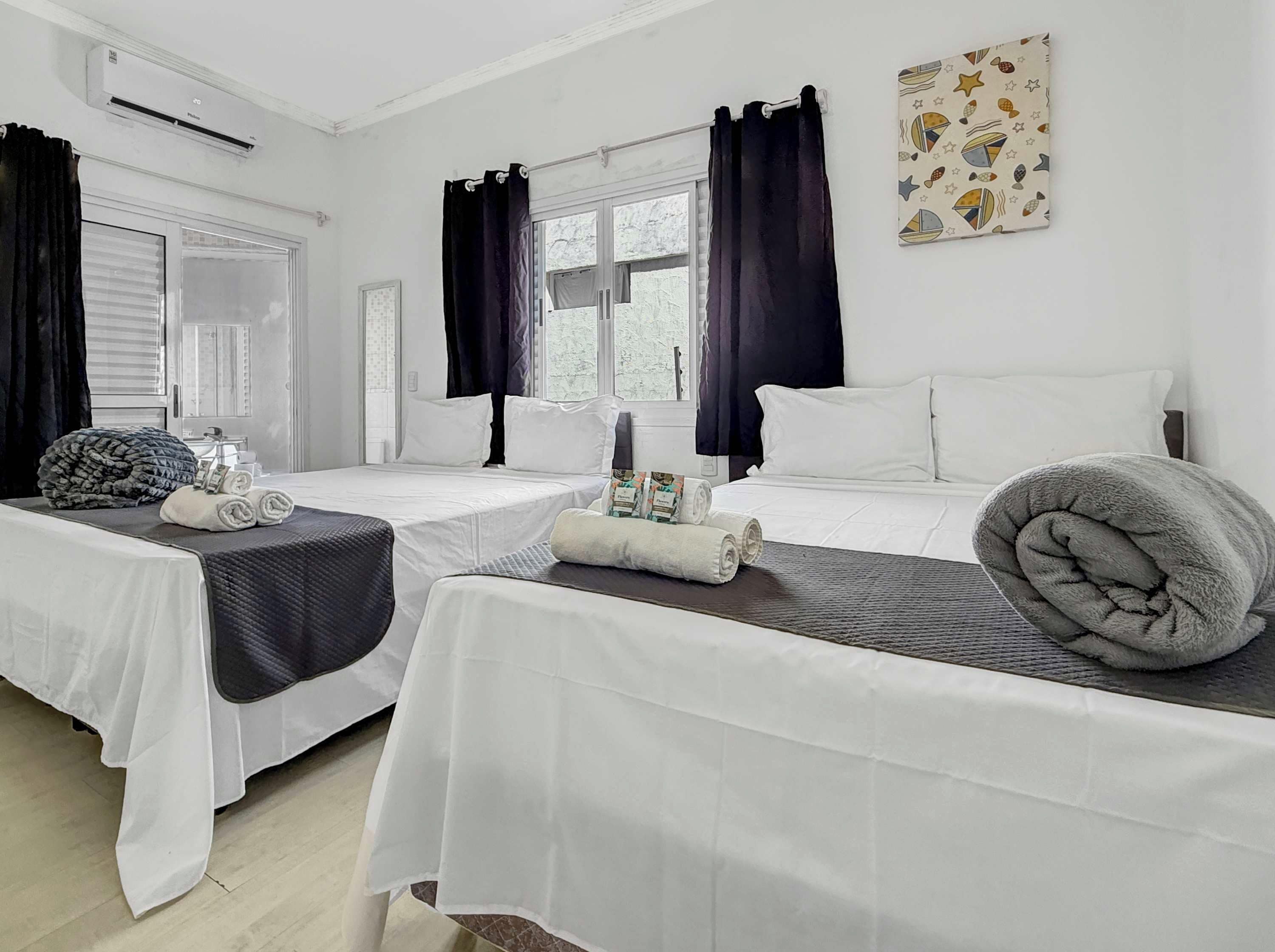 Habitación de hotel con dos camas, una ventana con cortinas, un equipo de aire acondicionado y una decoración en la pared.