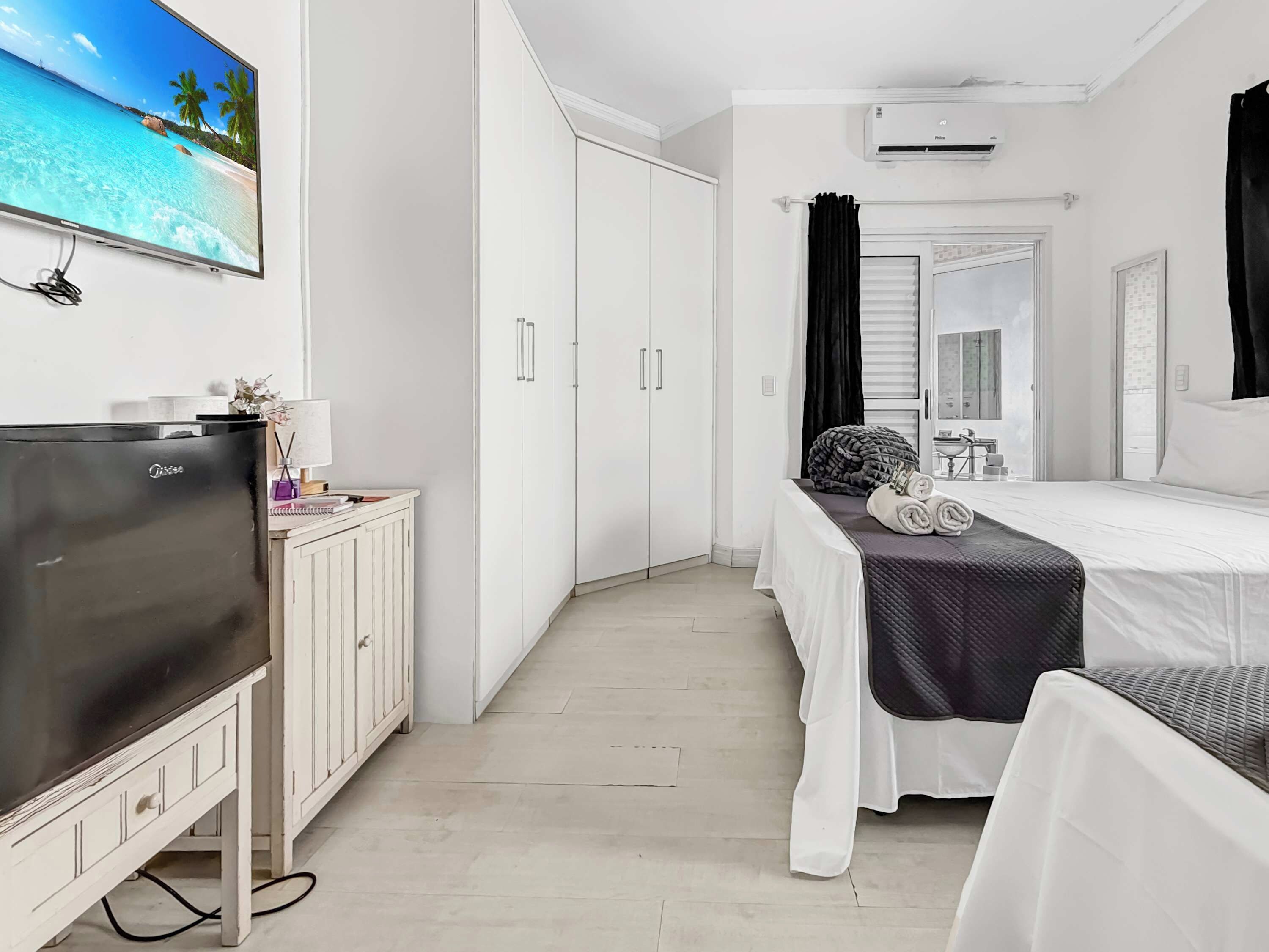 Une chambre d’hôtel comprenant un lit, une télévision, une armoire et une salle de bain avec un miroir et un lavabo.