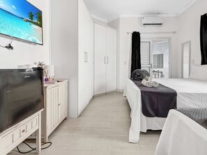 Habitación de hotel con cama, televisión, armario y baño con espejo y lavamanos.