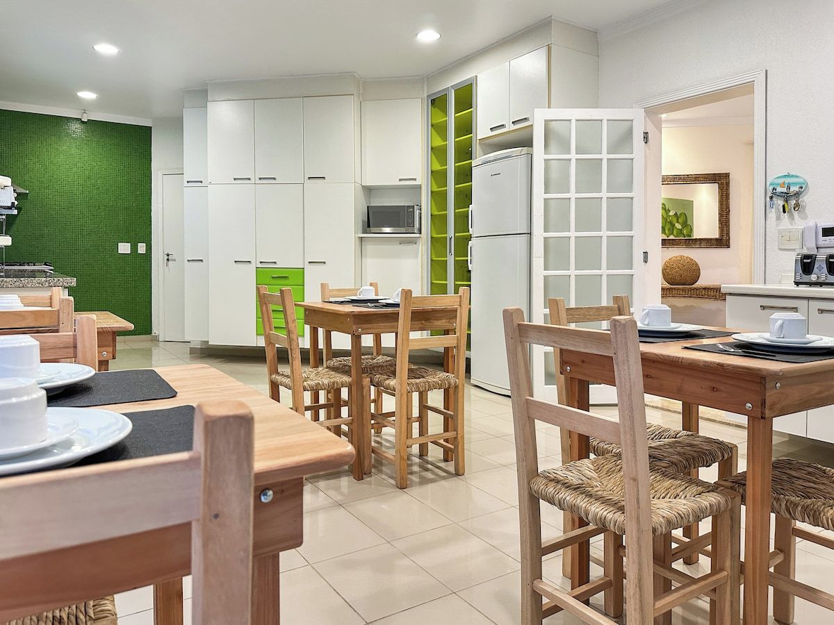 A modern kitchen with white cabinets, a green accent wall, and a dining area with wooden chairs and tables.