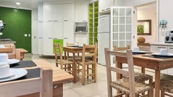 A modern kitchen with white cabinets, a green accent wall, and a dining area with wooden chairs and tables.