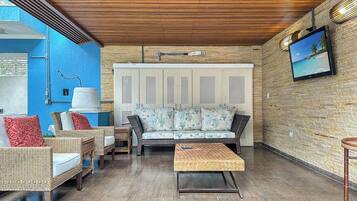 A room with a sofa, chairs, a coffee table, a TV, and a wall with a screen.