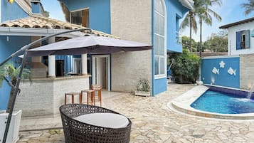 A poolside area with a stone floor, outdoor seating, and a pool with a blue border.