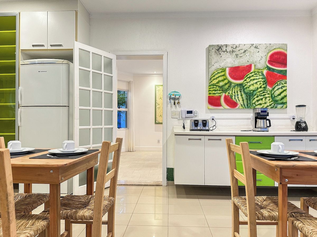 A modern kitchen with a dining area, white cabinets, a microwave, and a painting of watermelons on the wall.