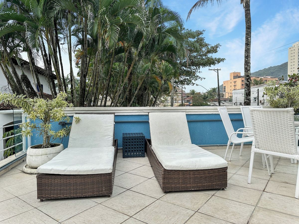 A rooftop terrace with two lounge chairs, a small table, and a potted plant.