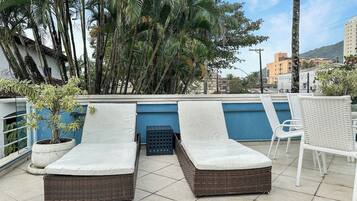 A rooftop terrace with two lounge chairs, a small table, and a potted plant.