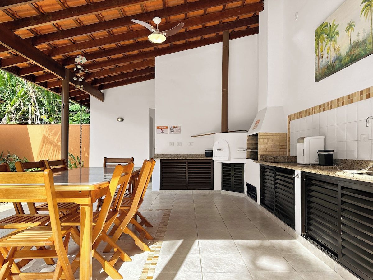 Cozinha e sala de jantar integradas, com ventoinha no teto, forno a pizza e mesa com cadeiras.