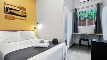 Quarto de hotel com cama, escrivaninha, cadeira e janela com cortinas.