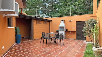 An outdoor patio with a barbecue grill, a table with chairs, and a potted plant.