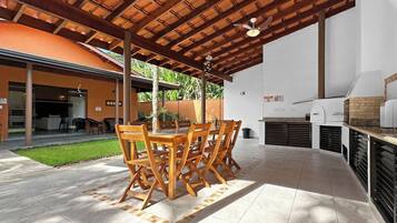 An outdoor patio with a wooden table and chairs, a barbecue grill, and a covered area with a ceiling fan.