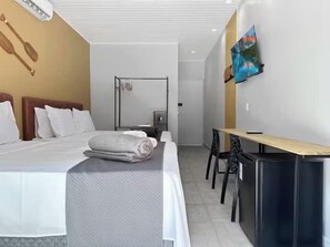 A hotel room with a bed, a desk, a chair, a television, and a wall-mounted artwork. - 200m da praia - AC - Suite com frigobar - Jacuzzi (Guarujá)