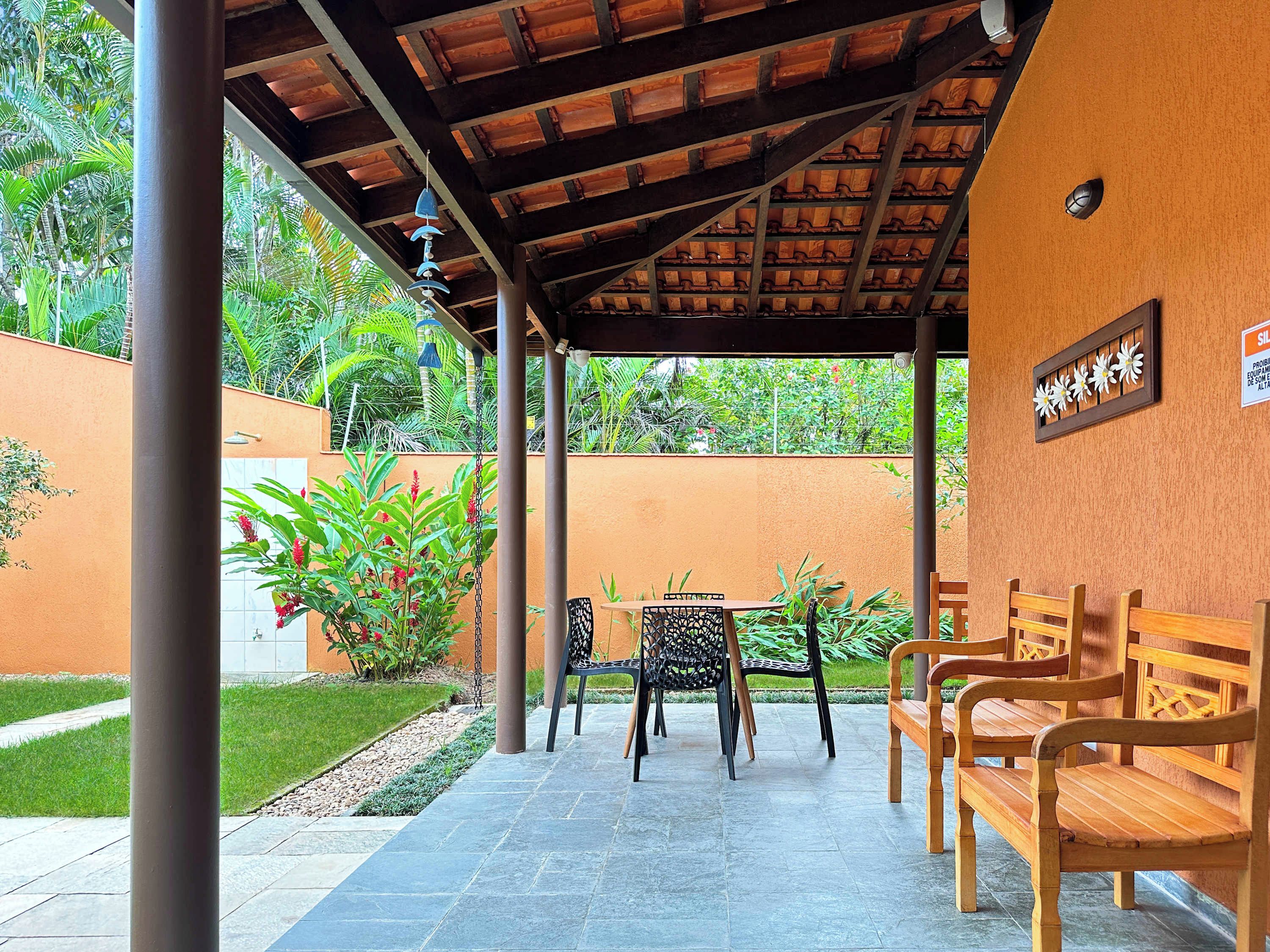 An outdoor seating area with a covered patio, stone flooring, and wooden benches.