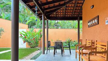 An outdoor seating area with a covered patio, stone flooring, and wooden benches.
