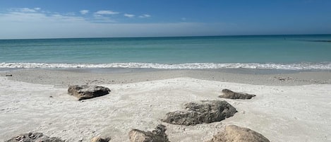 Una playa con rocas grandes al frente y mar tranquilo bajo un cielo despejado.