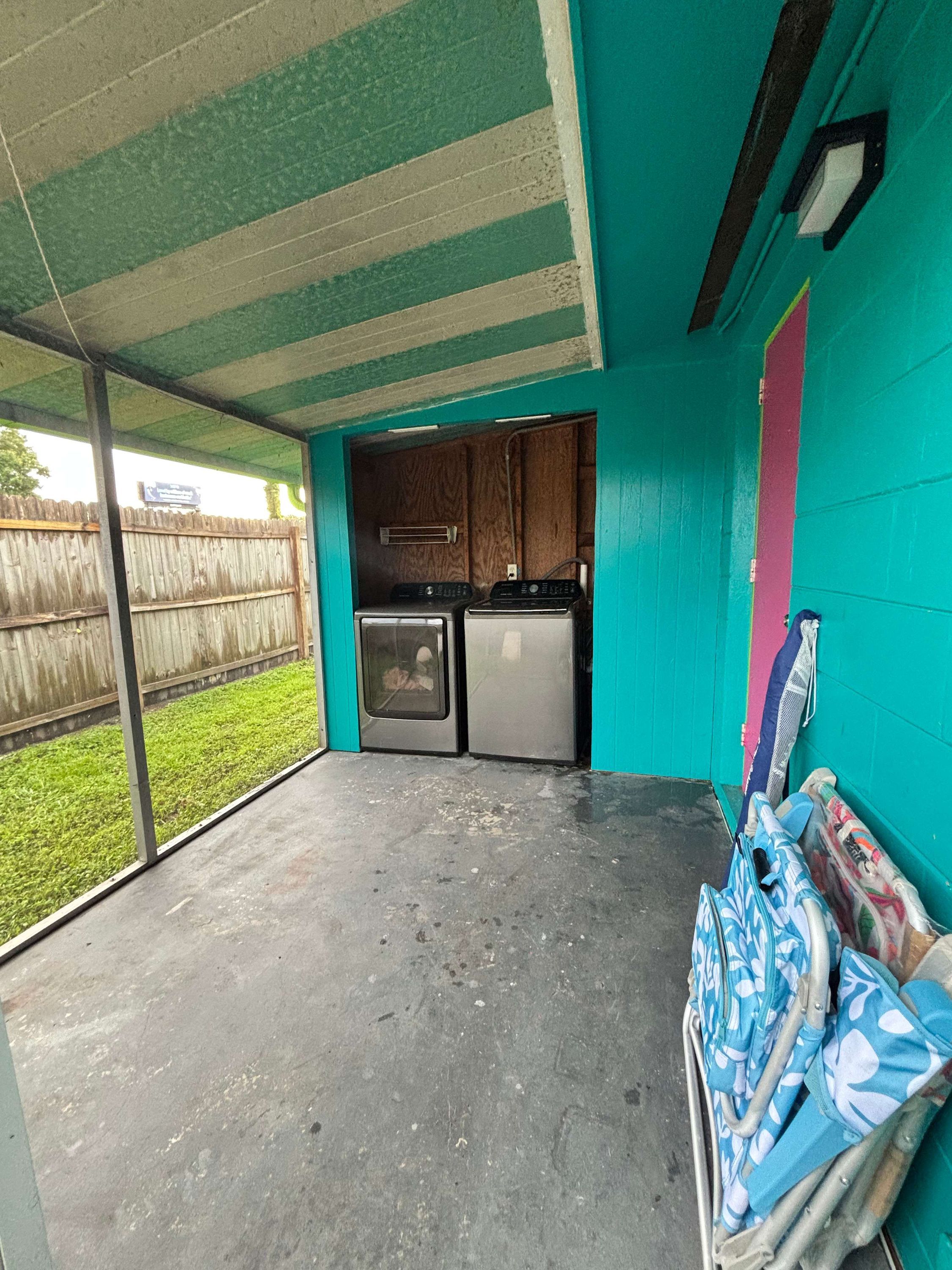 A covered outdoor area with a kitchenette, a concrete floor, and a view of a grassy yard.