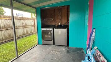 A covered outdoor area with a kitchenette, a concrete floor, and a view of a grassy yard.