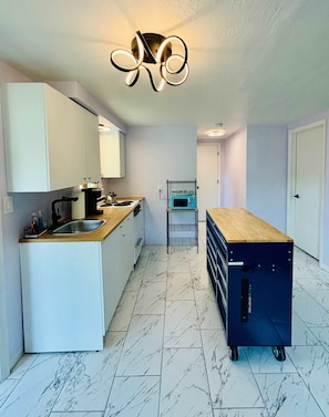 Una cocina moderna con armarios blancos, encimera de madera, horno empotrado y un microondas en un estante.
