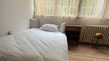 A bedroom with a bed, a nightstand, a radiator, and a window with curtains.