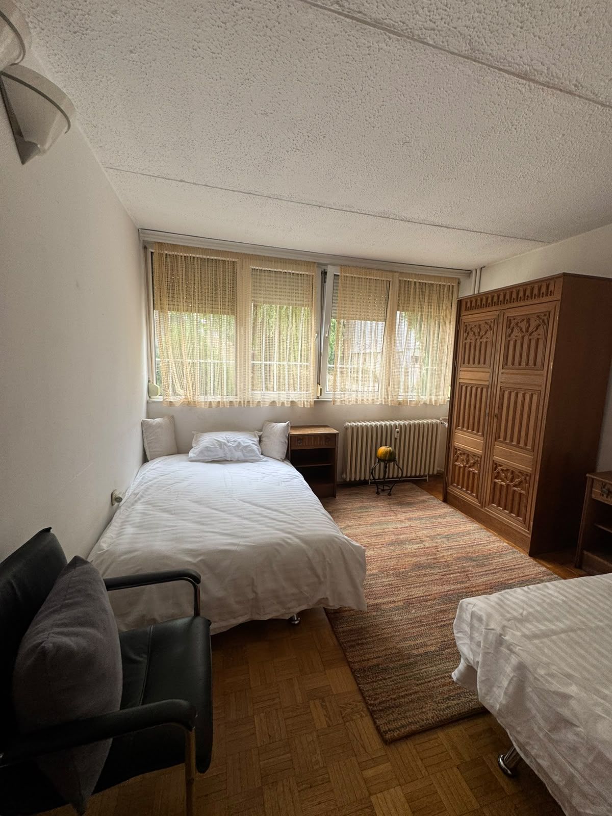 Un dormitorio con dos camas, un radiador, un armario de madera y una silla.
