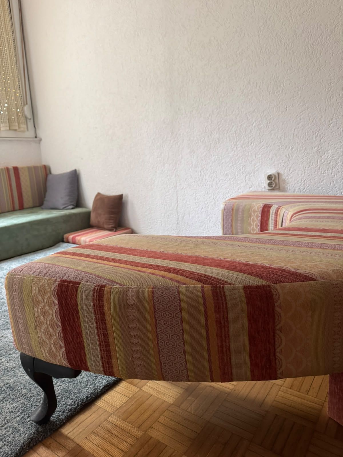 A room with a wooden floor, a sofa with a striped cushion, and a bed with a patterned bedspread.