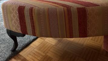 A room with a wooden floor, a sofa with a striped cushion, and a bed with a patterned bedspread.