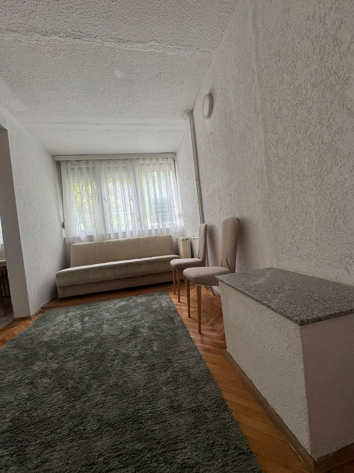 Una sala de estar con un sofá, sillas, una mesita y una ventana con cortinas.
