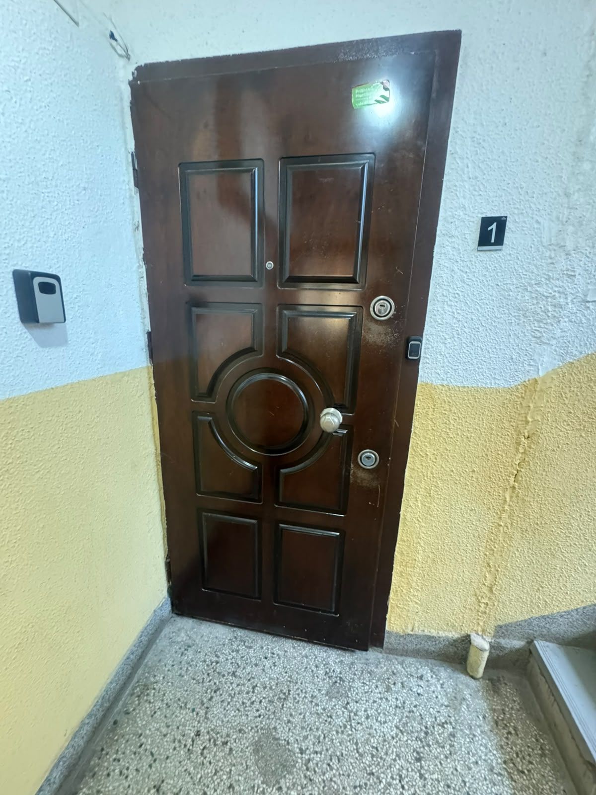 A brown door with a circular center panel and four square panels, a keyhole, and a doorbell.