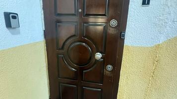 A brown door with a circular center panel and four square panels, a keyhole, and a doorbell.