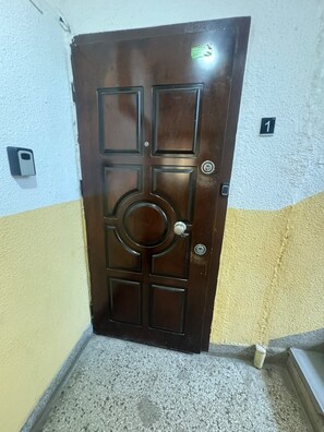 A brown door with a circular center panel and four square panels, a keyhole, and a doorbell. - Lorik Apartment (Prishtinë)