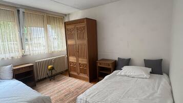 Ein Schlafzimmer mit zwei Betten, einem Holzschrank, einem Heizkörper und einem Fenster mit Vorhängen.