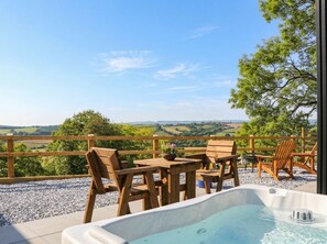 An outdoor seating area with a hot tub, wooden furniture, and a view of the countryside. - Little Folley (Exeter)