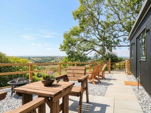 An outdoor patio with wooden furniture, a fire pit, and a view of the countryside. - Little Folley (Exeter)