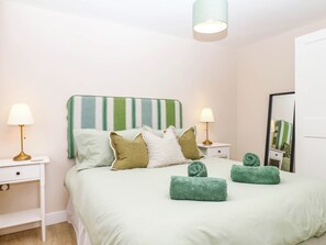 A neatly arranged bedroom with a bed, two bedside tables, a lamp, a mirror, and a green-striped headboard. - Little Folley (Exeter)