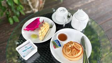 Un tavolo con una pila di pancake, un teiera, una tazza, un piccolo contenitore di zucchero bianco e una confezione di burro.