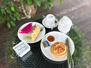 A table with a plate of pancakes, a teapot, a cup, a small container of white sugar, and a packet of butter.