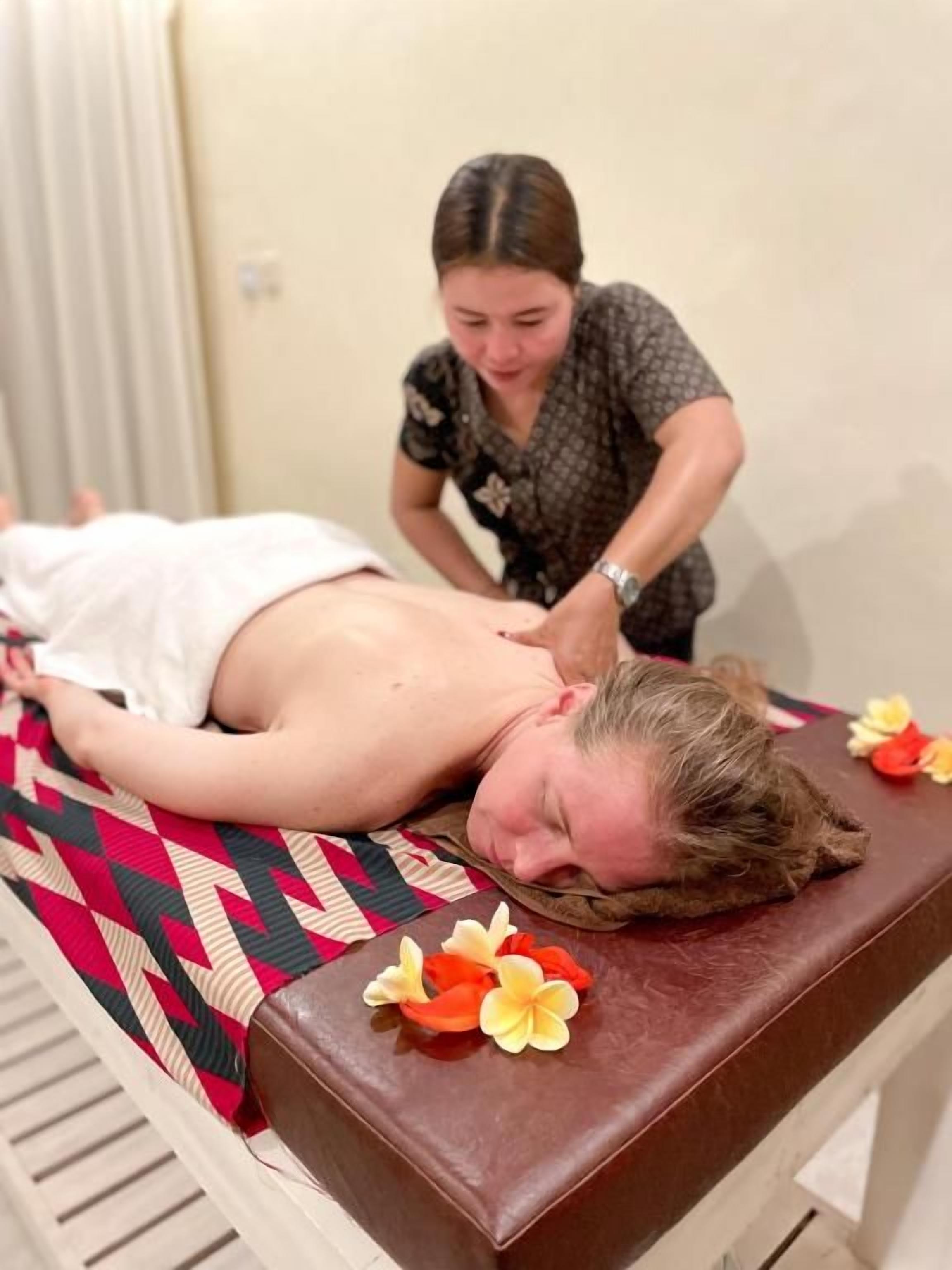 Eine Massageanwendung in einem Raum mit Liege, Massagetisch und Handtuch.