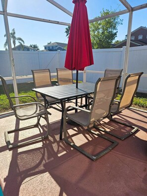 An outdoor patio with a table and chairs, a red umbrella, and a white fence in the background. - Disney Pool Escape | Game Room + Sleeps 14 (Davenport)