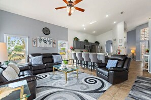 A modern living room with a black leather sofa, a glass coffee table, and a ceiling fan. - Disney Pool Escape | Game Room + Sleeps 14 (Davenport)