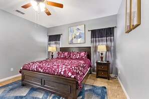 A bedroom with a bed, a ceiling fan, a nightstand, a lamp, and a painting on the wall. - Disney Pool Escape | Game Room + Sleeps 14 (Davenport)