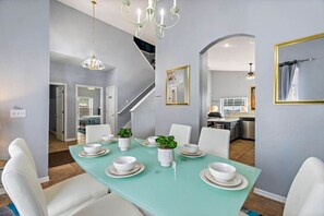A dining area with a teal table, white chairs, and a chandelier. There is a staircase leading to another room. - Disney Pool Escape | Game Room + Sleeps 14 (Davenport)