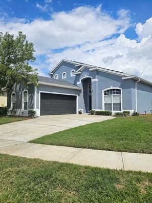 A two-story residential house with a garage, a front lawn, and a clear sky. - Disney Pool Escape | Game Room + Sleeps 14 (Davenport)