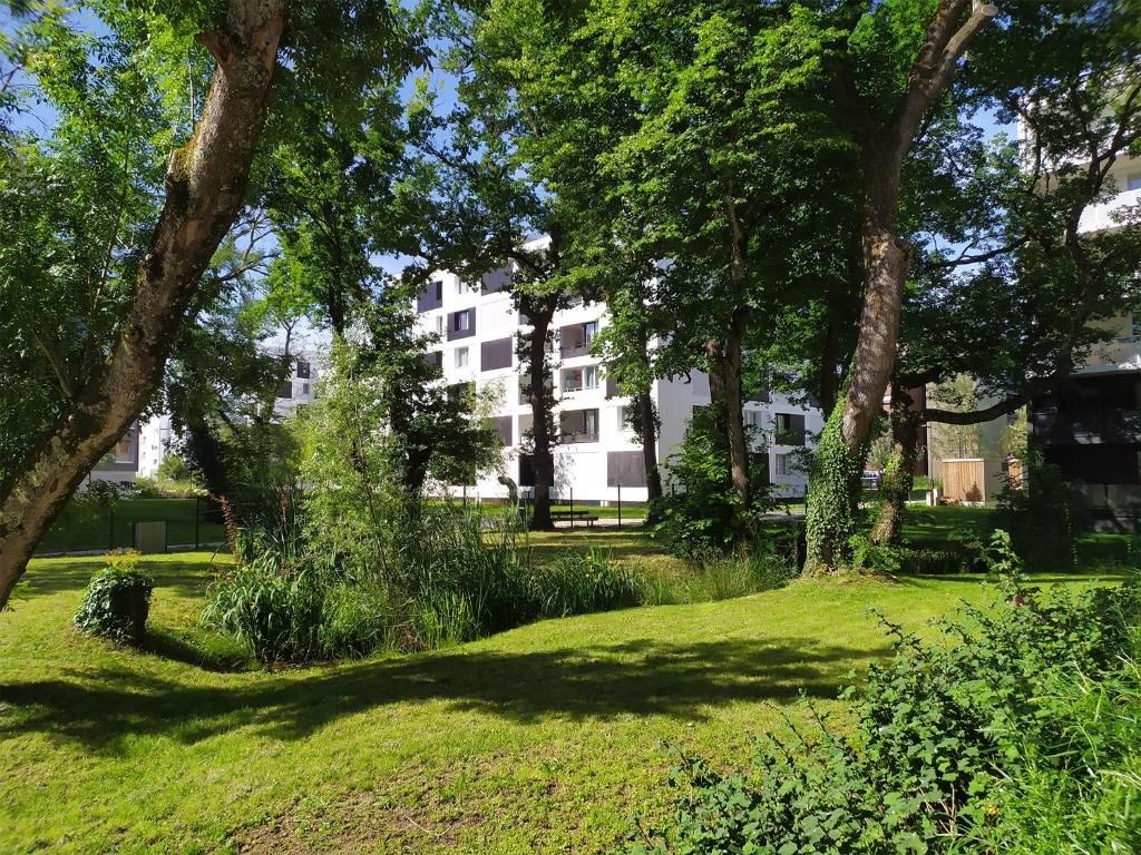 A residential building with multiple balconies, surrounded by lush greenery and trees.