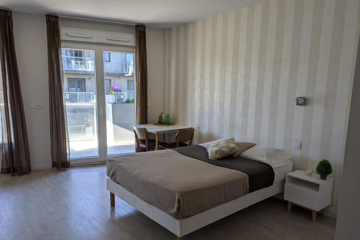 Un dormitorio con una cama, una mesita de noche, una silla y vistas al exterior mediante una puerta corredera.
