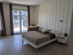 Un dormitorio con una cama, una mesita de noche, una silla y vistas al exterior mediante una puerta corredera.