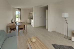 Un soggiorno moderno con un divano, un tavolo da pranzo e sedie. È presente una zona cucina con pensili e un lavello. Si vedono una lampada e un lampadario.