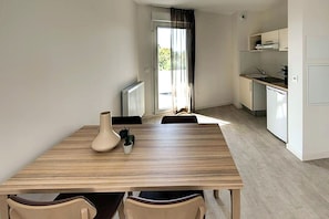 A modern kitchen with white cabinets, a dining table with chairs, and a view through a glass door. - Zenao Appart'hôtels Bègles (Bègles)