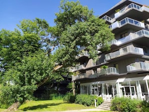 Un edificio residencial de varios pisos con balcones, césped y árboles.