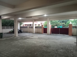 Un área de estacionamiento techada con piso pavimentado, una motocicleta y una entrada con portón.