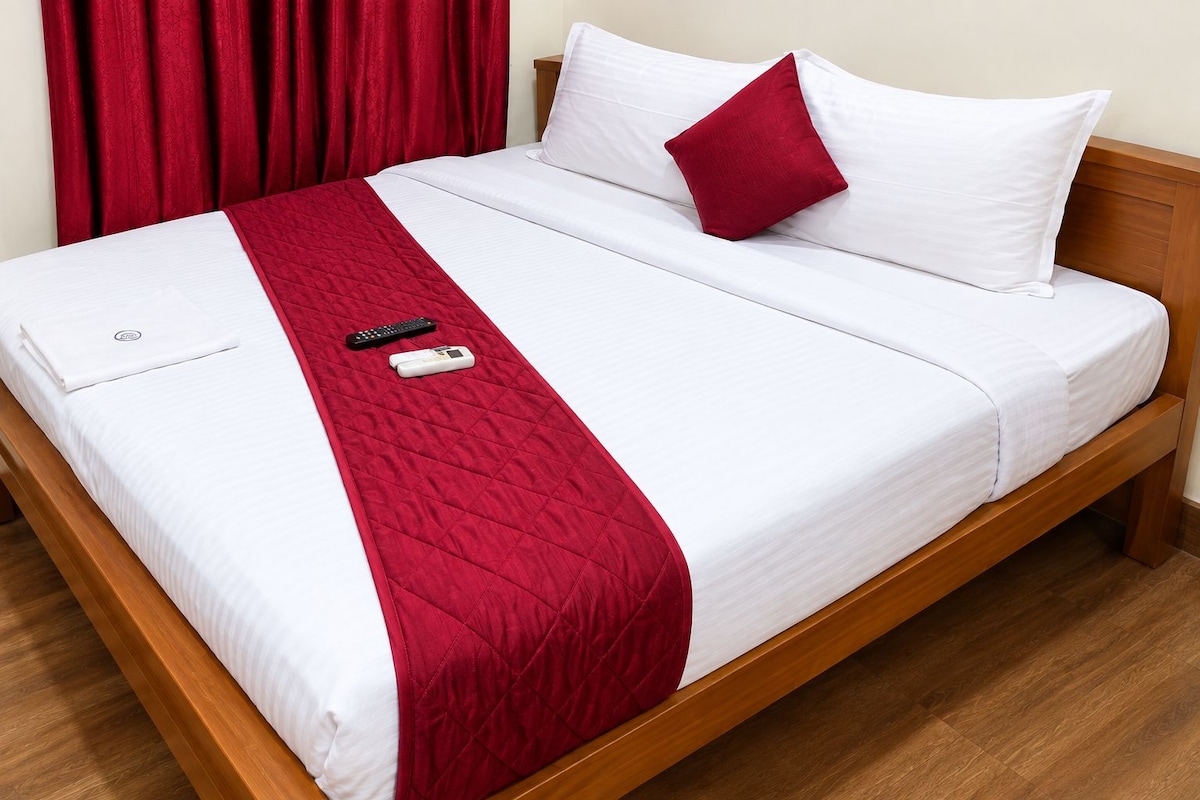 Una cama bien hecha con colcha roja, almohadas blancas y un control remoto sobre ella.